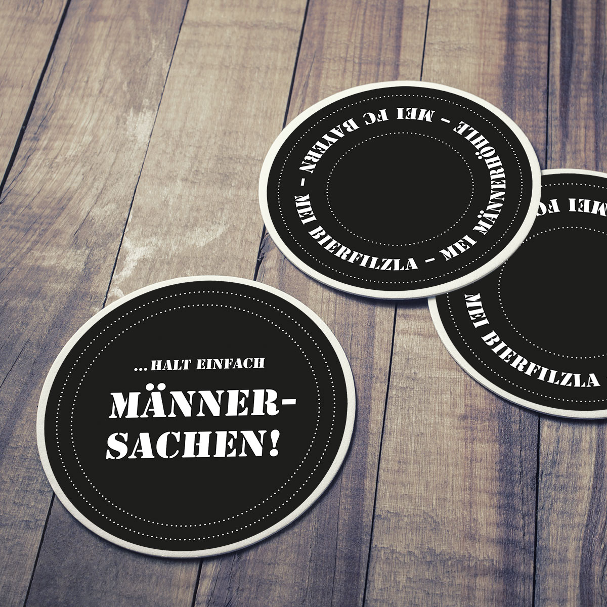 Teaser Quadrat verlinkt, schwarze Bierdeckel "Männersachen" mit weißen Randverzierungen und coolen Männersprüchen